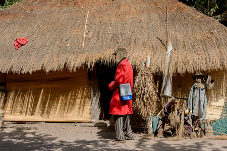 CANHABAQUE, GUINEA BISSAU - MAY 4, 2017: Unidentified local man with beard in a hat and red coat stands near the shack in a village of the Canhabaque island. People in G.-Bissau still suffer of povertyのeditorial素材