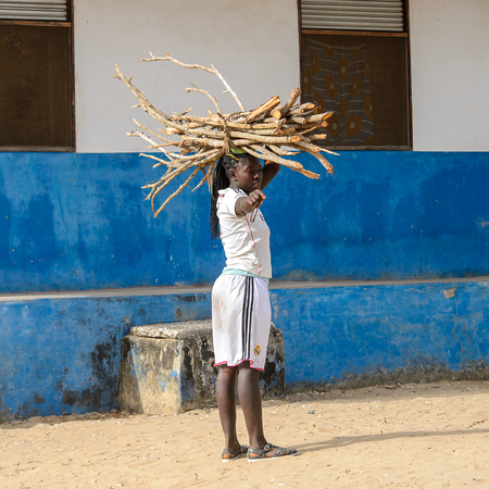 ORANGO ISLAND, GUINEA BISSAU - MAY 3, 2017: Unidentified local woman carries wooden sticks on her head in the Etigoca village. People in G.-Bissau suffer of poverty due to the bad economyのeditorial素材