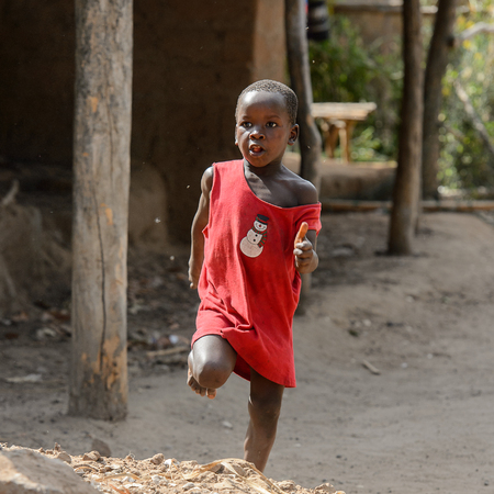 CANHABAQUE, GUINEA BISSAU - MAY 4, 2017: Unidentified local little boy in red shirt runs along the street in a village of the Canhabaque island. People in G.-Bissau still suffer of povertyのeditorial素材