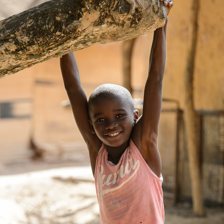 CANHABAQUE, GUINEA BISSAU - MAY 4, 2017: Unidentified local little boy in pink shirt hangs on the tree in a village of the Canhabaque island. People in G.-Bissau still suffer of povertyのeditorial素材