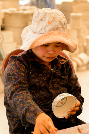 HANOI, VIETNAM - SEP 24, 2014: Unidentified Vietnamese woman draws on the ceramic dish in the ceramic workshop. Ceramic art is very popular in Asian cultureのeditorial素材