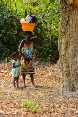 SOGA, GUINEA BISSAU - MAY 5, 2017: Unidentified local woman in colored clothes carries a basin on her head in a village of the Soga island. People in G.-Bissau still suffer of povertyのeditorial素材