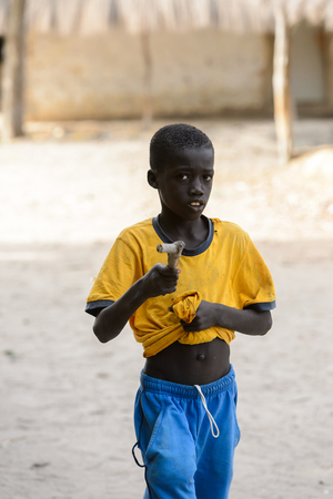 ORANGO ISLAND, GUINEA BISSAU - MAY 3, 2017: Unidentified local little boy walks with wooden stick in the Etigoca village. People in G.-Bissau suffer of poverty due to the bad economyのeditorial素材