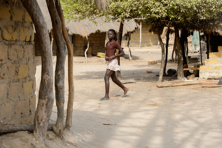 ORANGO ISLAND, GUINEA BISSAU - MAY 3, 2017: Unidentified local woman with braids walks along the street in the Etigoca village. People in G.-Bissau suffer of poverty due to the bad economyのeditorial素材