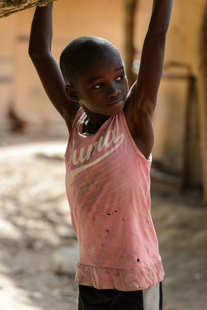 CANHABAQUE, GUINEA BISSAU - MAY 4, 2017: Unidentified local little boy in pink shirt hangs on the tree in a village of the Canhabaque island. People in G.-Bissau still suffer of povertyのeditorial素材