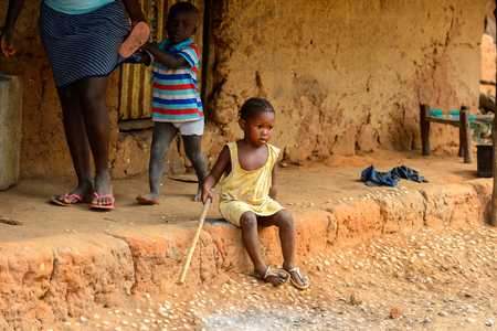SOGA, GUINEA BISSAU - MAY 5, 2017: Unidentified local little girl sits on the ground with a wooden stick in a village of the Soga island. People in G.-Bissau still suffer of povertyのeditorial素材