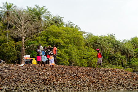 SOGA, GUINEA BISSAU - MAY 5, 2017: Unidentified local woman in red shirt and headscarf walks on the coast of the Soga island, part of the Bijagos Archipelagoのeditorial素材