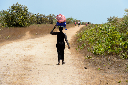 ORANGO ISLAND, GUINEA BISSAU - MAY 3, 2017: Unidentified local woman carries a bag on her head in the Etigoca village. People in G.-Bissau suffer of poverty due to the bad economyのeditorial素材