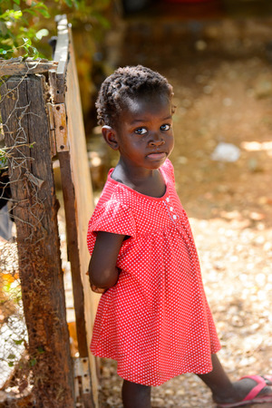 BUBAQUE, GUINEA BISSAU - MAY 5, 2017: Unidentified local little girl in red dress stands near the fence in a village of the Bubaque island. People in G.-Bissau still suffer of povertyのeditorial素材