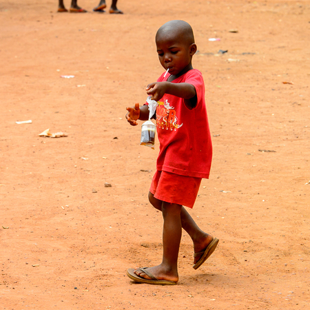 BUBAQUE, GUINEA BISSAU - MAY 5, 2017: Unidentified local little boy in red suit walks along the street in a village of the Bubaque island. People in G.-Bissau still suffer of povertyのeditorial素材