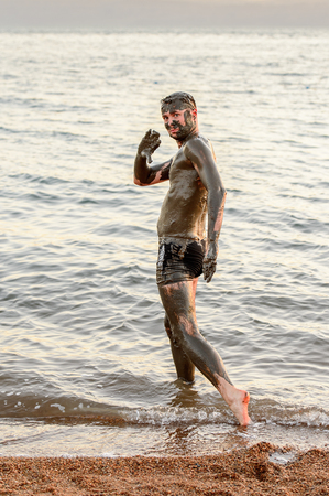 DEAD SEA RESORT, JORDAN - APR 30, 2014: Unidentified man in Dead Sea mud poses for the camera. The mud of Dead Sea is being used with the therapy purposses for the people with skin problemsのeditorial素材