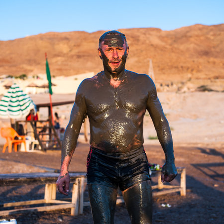 DEAD SEA RESORT, JORDAN - APR 30, 2014: Unidentified man in Dead Sea mud poses for the camera. The mud of Dead Sea is being used with  the therapy purposses for the people with skin problemsのeditorial素材