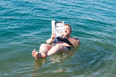 DEAD SEA RESORT, JORDAN - MAY 1, 2014: Unidentified woman reads a book laying on the water surface of the Dead Sea. Dead Sea water is used for medical purposes for the people with skin problemsのeditorial素材