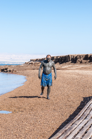 DEAD SEA RESORT, JORDAN - APR 30, 2014: Unidentified man in a Dead Sea mud walks on the beach. Dead Sea mud posesses the medical qualitiesのeditorial素材