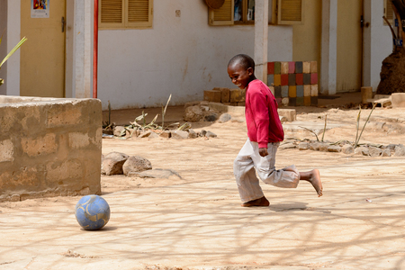 DAKAR, SENEGAL - APR 27, 2017: Unidentified Senegalese little boy in pink jamper and white pants plays football on the ground in the Village des Arts in Dakarのeditorial素材