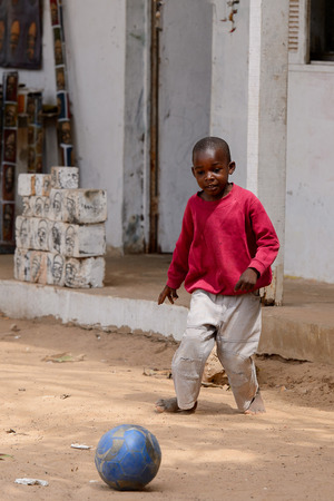 DAKAR, SENEGAL - APR 27, 2017: Unidentified Senegalese little boy in pink jamper and white pants plays football on the ground in the Village des Arts in Dakarのeditorial素材