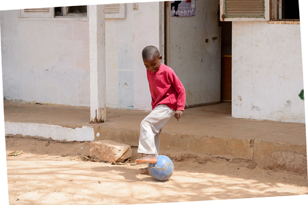 DAKAR, SENEGAL - APR 27, 2017: Unidentified Senegalese little boy in pink jamper and white pants plays football on the ground in the Village des Arts in Dakarのeditorial素材