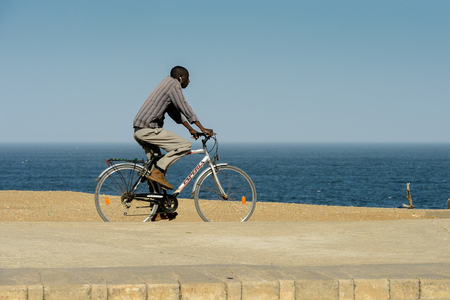 DAKAR, SENEGAL - APR 23, 2017: Unidentified Senegalese man rides a bicycle on the beach in Dakar, the capital and main city of Senegalのeditorial素材