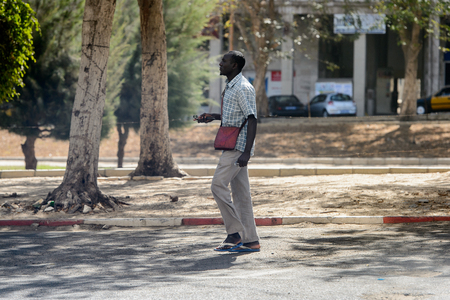 DAKAR, SENEGAL - APR 23, 2017: Unidentified Senegalese man in plaid shirt walks beside the road in Dakar, the capital and main city of Senegalのeditorial素材