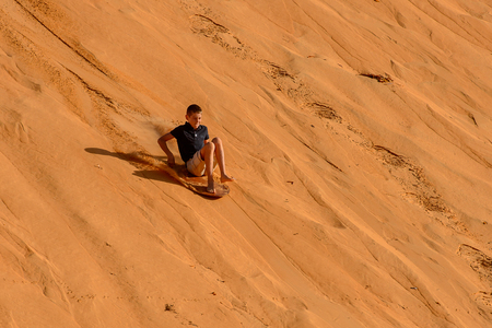LAMPOUL DESERT, SENEGAL - APR 23, 2017: Unidentified tourist's little boy rides on the board from the top of sand dune in a Lampoul Desert, beautiful landscape placeのeditorial素材