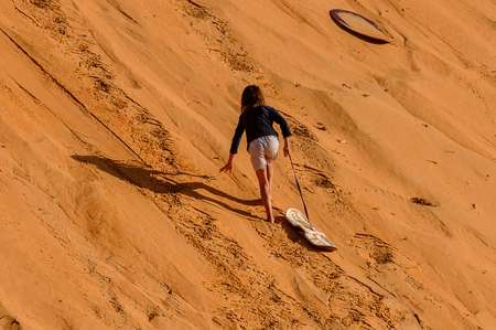 LAMPOUL DESERT, SENEGAL - APR 23, 2017: Unidentified tourist's little girl walks with the board to the top of sand dune in a Lampoul Desert, beautiful landscape placeのeditorial素材