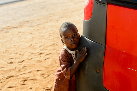 ROAD TO LAMPOUL, SENEGAL - APR 23, 2017: Unidentified Senegalese little boy leans on the bumper of the car. Still many people in Senegal live in povertyのeditorial素材