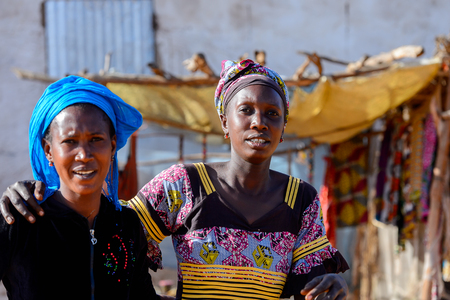 LAMPOUL DESERT village, SENEGAL - APR 23, 2017: Unidentified Senegalese two women in colored clothes and headscarves hug each other in a village near the Lampoul Desertのeditorial素材