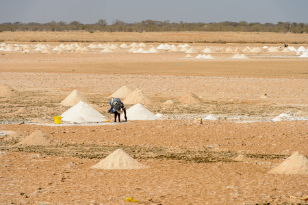 ROAD TO LAMPOUL, SENEGAL - APR 23, 2017: Unidentified Senegalese woman bends down near the heap of sand. Still many people in Senegal live in povertyのeditorial素材