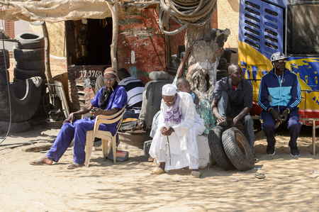 ROAD TO LAMPOUL, SENEGAL - APR 23, 2017: Unidentified Senegalese people sit around the tree trunk. Still many people in Senegal live in povertyのeditorial素材