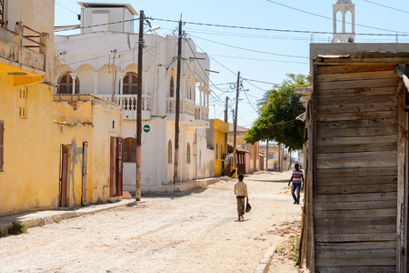 SAINT LOUIS, SENEGAL - APR 24, 2017: Unidentified Senegalese little boy walks with a plastic bag  along the street with beautiful architecture in Saint Louis, one of the biggest cities in Senegalのeditorial素材