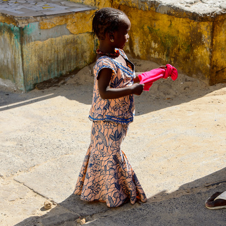 SAINT LOUIS, SENEGAL - APR 24, 2017: Unidentified Senegalese little girl with braids holds a pink scarf at the local market of Saint Louis, Senegalのeditorial素材