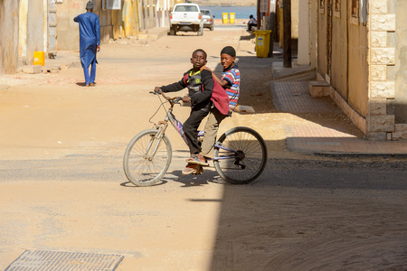 SAINT LOUIS, SENEGAL - APR 24, 2017: Unidentified Senegalese little boy rides his friend on a bicycle in Saint Louis, one of the biggest cities in Senegalのeditorial素材