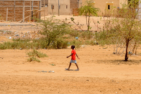 ROAD TO LAMPOUL, SENEGAL - APR 23, 2017: Unidentified Senegalese little boy in red shirt and grey shorts walks along the street. Still many people in Senegal live in povertyのeditorial素材