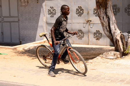 ROAD TO LAMPOUL, SENEGAL - APR 23, 2017: Unidentified Senegalese boy holds a bicycle. Still many people in Senegal live in povertyのeditorial素材