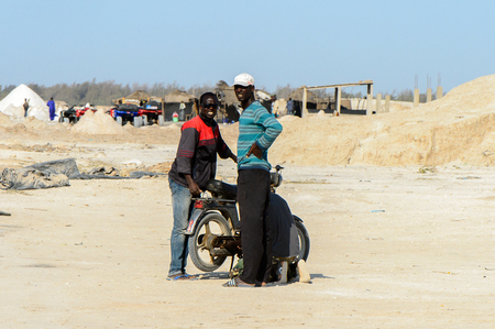LAC ROSE, SENEGAL - APR 26, 2017: Unidentified Senegalese two men stand near the motorcycle on the salty coast of the Lake Retba, UNESCO World Heritage Siteのeditorial素材