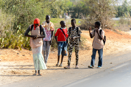 KAYAR, SENEGAL - APR 27, 2017: Unidentified Senegalese boys and a girl walk beside the road in a beautiful village near Kayar, Senegalのeditorial素材