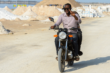 LAC ROSE, SENEGAL - APR 26, 2017: Unidentified Senegalese man rides a motorcycle on the salty coast of the Lake Retba, UNESCO World Heritage Siteのeditorial素材