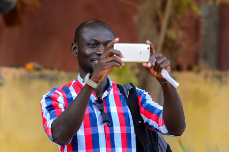 LAC ROSE, SENEGAL - APR 27, 2017: Unidentified Senegalese man in plaid shirt holds a cellphone on the Lake Retba, UNESCO World Heritage Siteのeditorial素材