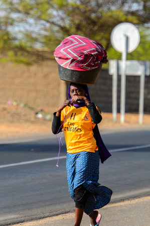 KAYAR, SENEGAL - APR 27, 2017: Unidentified Senegalese woman walks along the road with a basin on her head in a beautiful village near Kayar, Senegalのeditorial素材