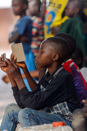 OUSSOUYE, SENEGAL - APR 30, 2017: Unidentified Senegalese little boys look at their cellphones in the Sacred Forest near Kaguit villageのeditorial素材