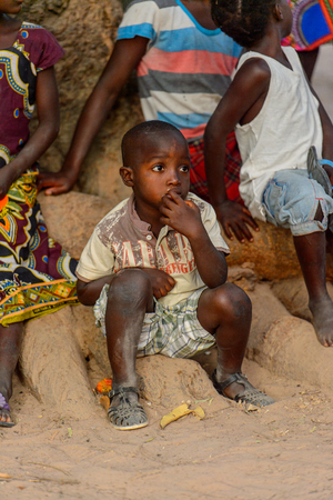 OUSSOUYE, SENEGAL - APR 30, 2017: Unidentified Senegalese little boy sits on the ground and puts his fingers into his mouth in the Sacred Forest near Kaguit villageのeditorial素材