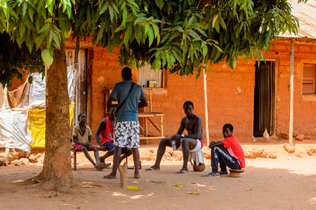 ROAD TO BISSAU, GUINEA B. - MAY 1, 2017: Unidentified local people sit under the tree in a village in Guinea Bissau. Still many people in the country live in povertyのeditorial素材