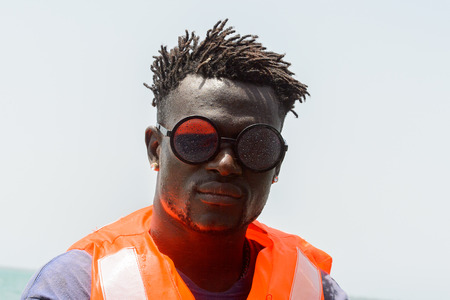 ORANGO ISLAND, GUINEA BISSAU - MAY 3, 2017: Unidentified local man in orange vest wears sunglasses and sails in a boat on the Orango Island, Guinea Bissauのeditorial素材