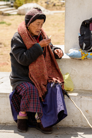 TRIMPHU, BHUTAN - MAR 8, 2017: Unidentified Ngalops old woman sits near the column on the street. Ngalops is one of the most populous ethnic groups of Bhutanのeditorial素材