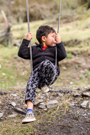TRIMPHU, BHUTAN - MAR 8, 2017: Unidentified Ngalops little boy rides a swing. Ngalops is one of the most populous ethnic groups of Bhutanのeditorial素材