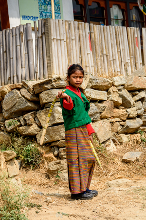 TRIMPHU, BHUTAN - MAR 8, 2017: Unidentified Ngalops little girl in traditional clothes walks with wooden sticks. Ngalops is one of the most populous ethnic groups of Bhutanのeditorial素材