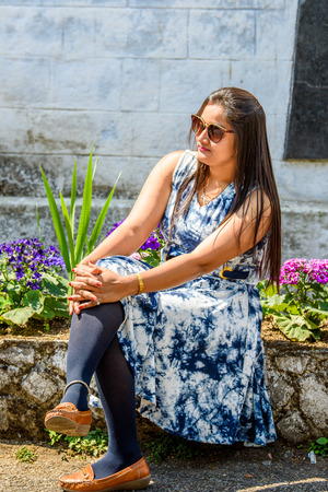 SIKKIM, INDIA - MAR 13, 2017: Unidentified Indian long-haired woman in sunglasses and colored dress sits near the flowerbed.のeditorial素材