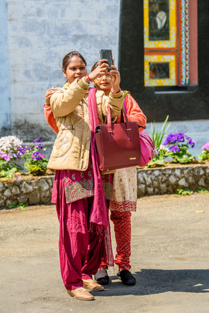 SIKKIM, INDIA - MAR 13, 2017: Unidentified Indian two girls in traditional clothes take a picture of themselves on a cellphone.のeditorial素材