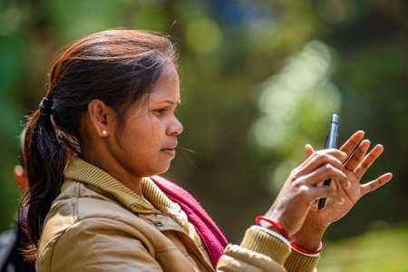 SIKKIM, INDIA - MAR 13, 2017: Unidentified Indian woman with pony tail wears an earing and mustard jacket tries to take a picture on her cellphone.のeditorial素材