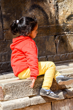 KATMANDU, NEPAL - MAR 6, 2017: Unidentified Chhetri little girl in red jamper and yellow pants sits on the street. Chhetris is the most populous ethnic group of Nepalのeditorial素材